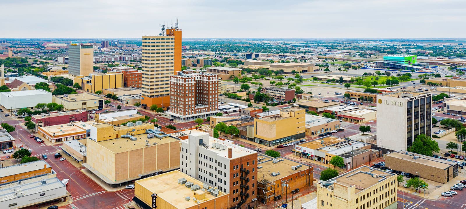 High-angle view of a sprawling city skyline with diverse buildings and a flat, distant horizon.
